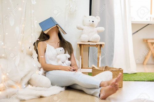 Beautiful Asian tired female student take a nap or sleep with book cover her face after hard reading